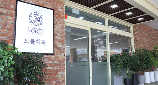 노블치과의원 출입구와 벽면 로고 간판, 유리 출입문 주변 모습